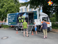 Drei Menschen stehen vor einem Lkw, an dem eine kleine Treppe zu einer offenen Tür führt.