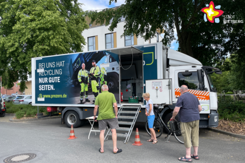 Drei Menschen stehen vor einem Lkw, an dem eine kleine Treppe zu einer offenen Tür führt.