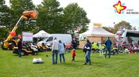 Auf einer Wiese besichtigen Besucher verschiedene Traktoren und Rasenmäher.