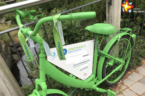 Ein grünes Fahrrad lehnt an einem Brückengeländer. Versehen ist das Rad mit einer Werbung für die Aktion Stadtradeln.