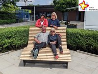 Andreas Pauleickhoff und Freibad-Chefin Kirsten Meier sitzen im Freibad auf einer überdimensionalen Liege, die mit dhellen dünnen Holzlatten versehen ist. Schwimmmeisterin Birgit Neugebauer und Doris Schulz von der städtischen Abteilung Schule, Kultur und Sport stehen lächelnd dahinter.