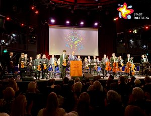 Ein ganzes Orchester erhebt sich auf der Bühne von ihren Stühlen.