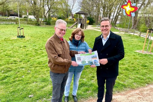 Die genannten Personen stehen am Rand der Rasenfläche, auf der sich der Spielplatz befindet und schauen in die Kamera.