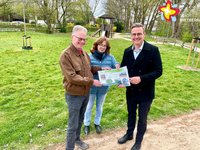 Die genannten Personen stehen am Rand der Rasenfläche, auf der sich der Spielplatz befindet und schauen in die Kamera.