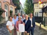 Die genannten Personen stehen zwischen Fachwerkhäusern, im Hintergrund ist die Klosterkirche zu sehen. Sie schauen in die Kamera.