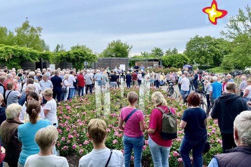 Etwa 50 Menschen stehen im Gartenschaupark zwischen Blumenbeeten und hören Bürgermeister Andreas Sunder zu.