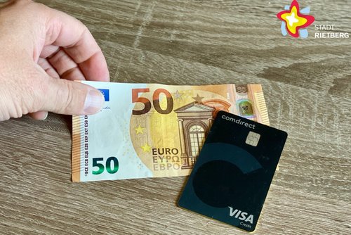 Eine Hand legt einen 50-Euro-Schein auf den Tisch, eine schwarze Visa-Karte liegt daneben.