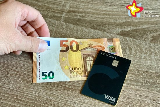 Eine Hand legt einen 50-Euro-Schein auf den Tisch, eine schwarze Visa-Karte liegt daneben.