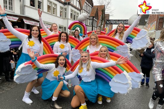 Zwölf junge Damen in blauen Röcken und weißen Pullis posieren mit farbigen Regenbogen auf die Rücken geschnallt für die Kamera.