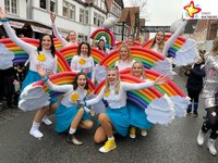 Zwölf junge Damen in blauen Röcken und weißen Pullis posieren mit farbigen Regenbogen auf die Rücken geschnallt für die Kamera.