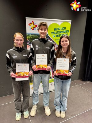 Zwei Mädchen und ein Junge in der Mitte stehen nebeneinader und halten Urkunden in den Händen.