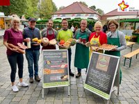 Die Rietberger Markthändler Sabrina Schmalhorst-Westhoff, Heinrich Buschsieweke, Bassel Ramadan, Florian Ebbesmeyer, Antonius Strunz, Birgit Kofort und Ulla Born stehen mit einigen ihrer Produkte in den Händen nebeneinander mitten auf dem Marktplatz.