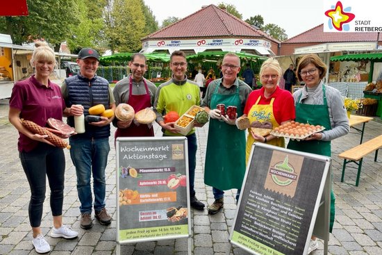 Die Rietberger Markthändler Sabrina Schmalhorst-Westhoff, Heinrich Buschsieweke, Bassel Ramadan, Florian Ebbesmeyer, Antonius Strunz, Birgit Kofort und Ulla Born stehen mit einigen ihrer Produkte in den Händen nebeneinander mitten auf dem Marktplatz.