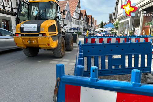 Das Foto zeigt die in Teilen abgesperrte Rathausstraße. Ein gelber Bagger fährt durch das Bild.
