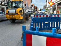 Das Foto zeigt die in Teilen abgesperrte Rathausstraße. Ein gelber Bagger fährt durch das Bild.