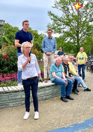 Anja Rodenbeck mit einem mikrofon in der Hand steht vor Andreas Sunder und Johannes Wiethoff. Daneben sitzen Besucher und hören zu.