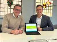 Zwei Männer sitzen nebeneinander, auf dem Tisch vor ihnen steht ein Tablet.