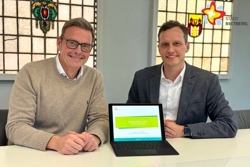 Zwei Männer sitzen nebeneinander, auf dem Tisch vor ihnen steht ein Tablet.