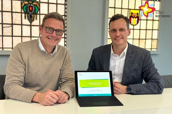 Zwei Männer sitzen nebeneinander, auf dem Tisch vor ihnen steht ein Tablet.