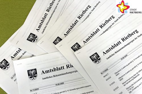 Mehrere gedruckte Amtsblätter liegen quer übereinander auf einem grünen Tisch.