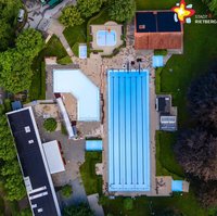 Zu sehen ist das Freibad aus der Vogelperspektive. In der Mitte des Fotos strahlt das hellblaue Becken. Rundherum ist es grün.