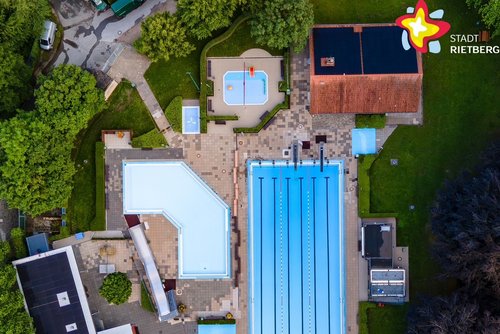 Zu sehen ist das Freibad aus der Vogelperspektive. In der Mitte des Fotos strahlt das hellblaue Becken. Rundherum ist es grün.