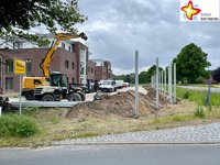 Zwischen einer Reihe Wohnhäuser und der Wiedenbrücker Straße hebt ein Bagger eine Tragsäule für die neue Schutzwand nach der anderen in den Boden, die nun wie Spargel aufgereiht aus dem Boden "sprießen".