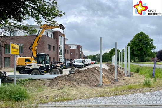 Zwischen einer Reihe Wohnhäuser und der Wiedenbrücker Straße hebt ein Bagger eine Tragsäule für die neue Schutzwand nach der anderen in den Boden, die nun wie Spargel aufgereiht aus dem Boden "sprießen".