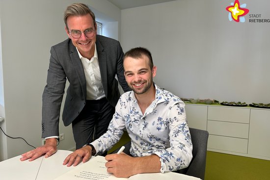 Bürgermeister Andreas Sunder schaut Erik Horsthemke über die Schulter. Dieser trägt sich ins Goldene Buch ein. Beide schauen in die Kamera.