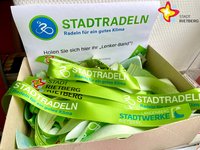 In einer Kiste liegen mehrere grüne Bänder mit der Aufschrift "Stadtradeln" durcheinander.