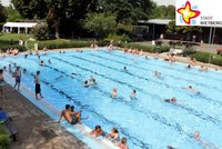 Ein Sommertag im Freibad. Badegäste schwimmen im Becken. Die Sonne scheint.