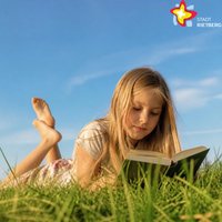 Ein Mädchen liegt auf einer Wiese und liest ein Buch. Der Himmel ist blau.