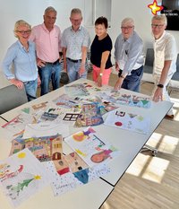 Sechs Frauen und Männer stehen rund um einen Tisch, der bedeckt ist mit gemalten Bildern.