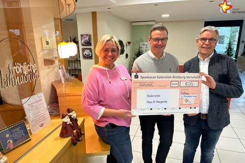 Die genannten Personen stehen im Foyer des Altenheims und halten einen großen Scheck in die Kamera.