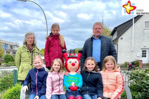 Lia, Jule, Ida, Pia und Marlene sitzen unter freiem Himmel auf einer Bank - die Rieti-Figur »Westi« in der Mitte. Kunstwerkstatt-Leiterin Karin Wolf und Wilfried Dörhoff von der Stadt Rietberg stehen links und rechts daneben und blicken ebenfalls in die Kamera.