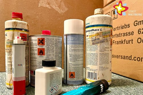 Mehrere sichtbar gebrauchte Spray- und Lackdosen stehen nebeneinander vor einem Pappkarton.