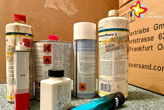 Mehrere sichtbar gebrauchte Spray- und Lackdosen stehen nebeneinander vor einem Pappkarton.