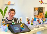 Julia Bröckling hat einige der Figuren vor sich auf einem Tisch stehen und schaut in die Kamera.