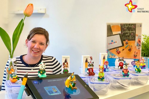 Julia Bröckling hat einige der Figuren vor sich auf einem Tisch stehen und schaut in die Kamera.