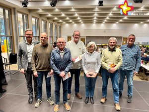 Sechs Männer und eine Frau stehen nebeneinander auf einer Bühne und schauen in die Kamera.