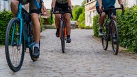 Drei Rennräder rollen über eine Kopfsteinpflasterstraße. Jedoch sind nur die Beine der Fahrer zu sehen.