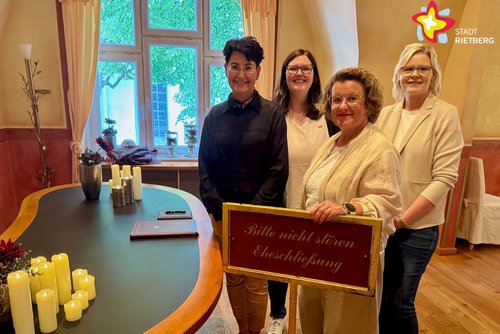 Vier Frauen stehen neben einem geschwungenen Tisch mit Kerzen darauf.