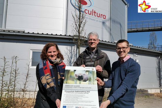 Klimaschutzmanagerin Svenja Schröder, Michael Kaune aus der Abteilung Hochbau und Gartenschaupark-Geschäftsführer Johannes Wiethoff stehen mit einem Plakat in der Hand vor der Cultura, im Hintergrund ist ein neu gepflanzter Baum zu sehen.