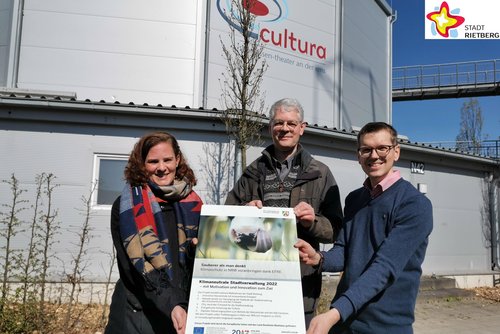 Klimaschutzmanagerin Svenja Schröder, Michael Kaune aus der Abteilung Hochbau und Gartenschaupark-Geschäftsführer Johannes Wiethoff stehen mit einem Plakat in der Hand vor der Cultura, im Hintergrund ist ein neu gepflanzter Baum zu sehen.
