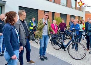 Klimaschutzmanagerin Svenja Schröder, Firmenchef Martin Holtermann und Bürgermeister Andreas Sunder begrüßen die Radler mit einem Mikrofon vor dem Firmengebäude von Holtermann Regeltechnik.