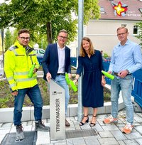 Jan Stephan, Bürgermeister Andreas Sunder, Dr. Gesa Kutschera und Dr. Carsten Behlert stehen hinter einem Trinkwasserspender an einem Radweg. Jeder hält eine grüne Flasche in der Hand, die sie mit Wasser füllen.