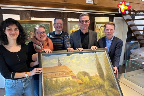 Die genannten Personen halten ein Ölgemälde in die Kamera und lächeln. Es zeigt das Rietberger Kloster. Im Hintergrund hängen drei weitere Bilder an einer Wand.