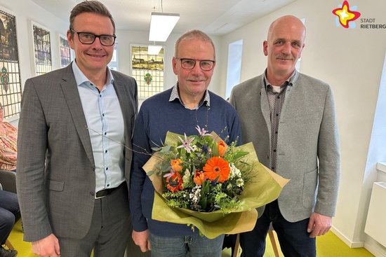 Bürgermeister Andreas Sunder, Jubilar Stefan Knapp mit Blümchen und Michael Schlüter vom Personalrat stehen nebeneinander.