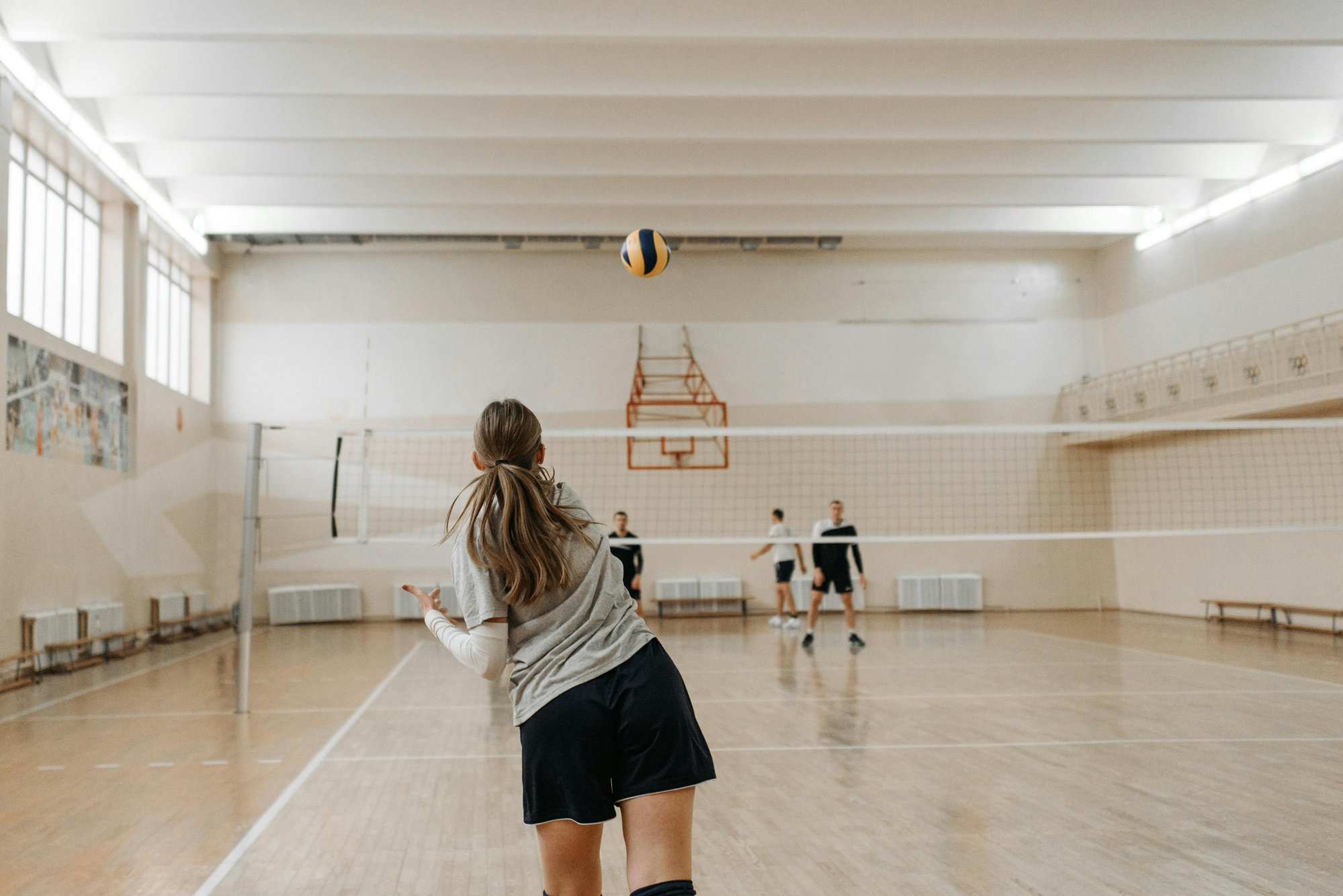 In einer Sporthalle dreht eine Sportlerin, die gerade einen Ball über ein Volleyballnetz geschlagen hat, den Rücken zu.