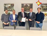 Fünf Männer stehen nebeneinande hinter einem Tisch. Der Mann in der Mitte hält eine Urkunde in den Händen.